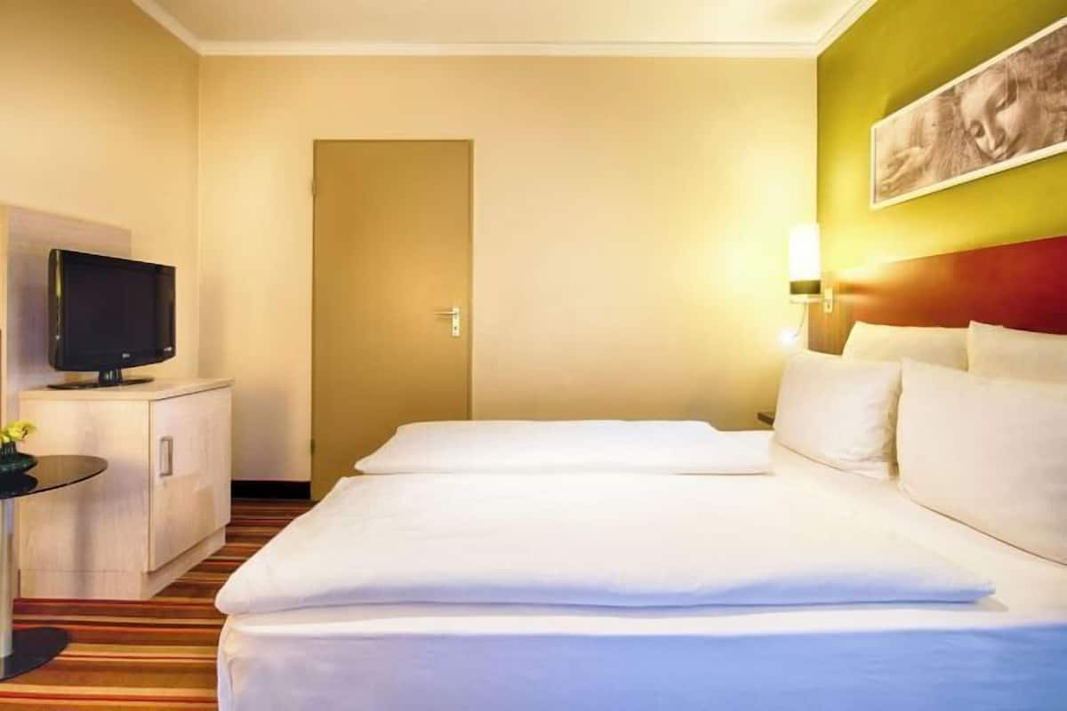 A hotel room with a bed, a television, a desk, and a painting on the wall.