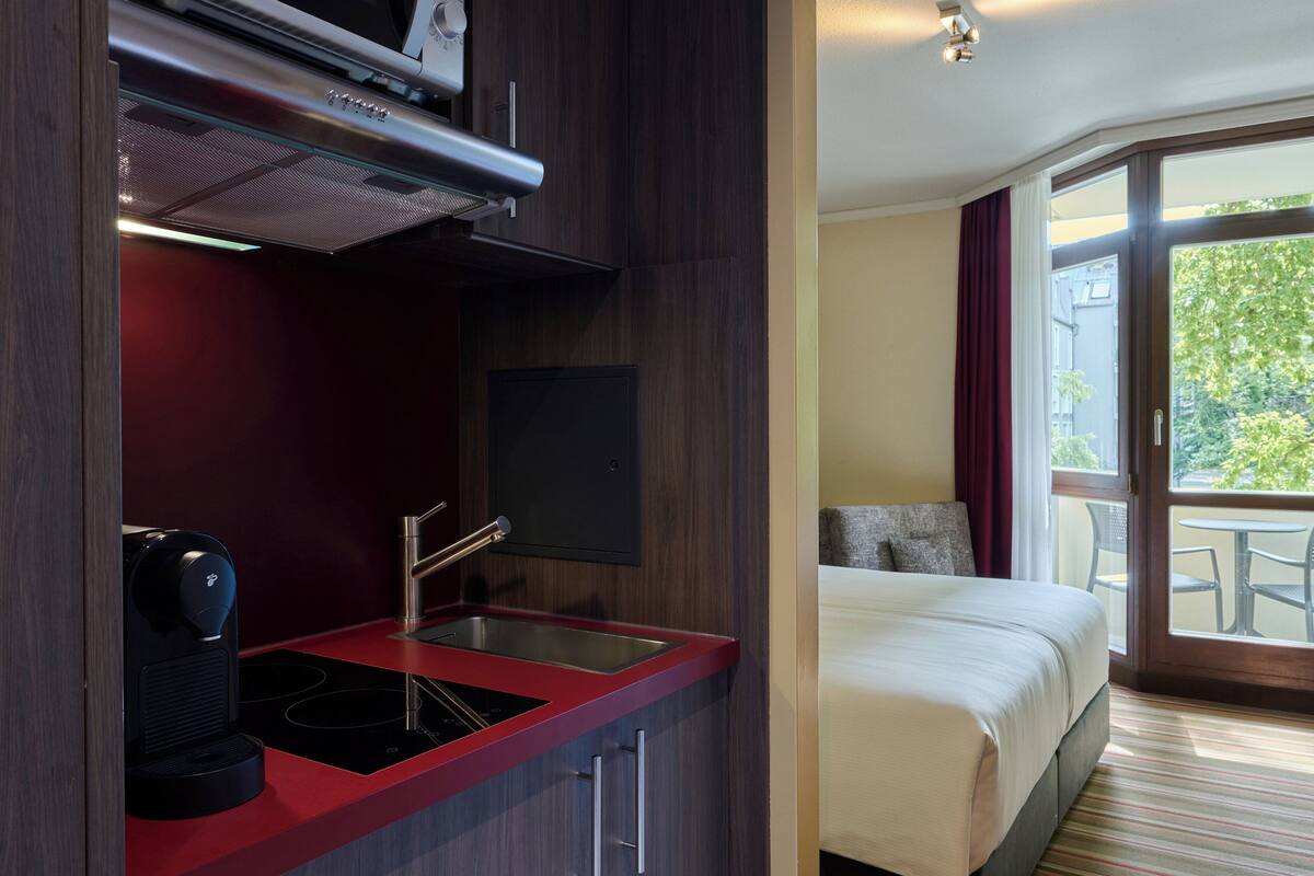 Una habitación de hotel moderna con kitchenette, una cama y un balcón con mobiliario exterior.