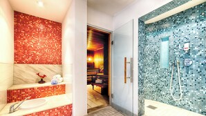 A bathroom with a red mosaic tile wall, a white sink, and a glass shower enclosure with a blue mosaic tile wall. - Leonardo Hotel & Residenz München (Munich)