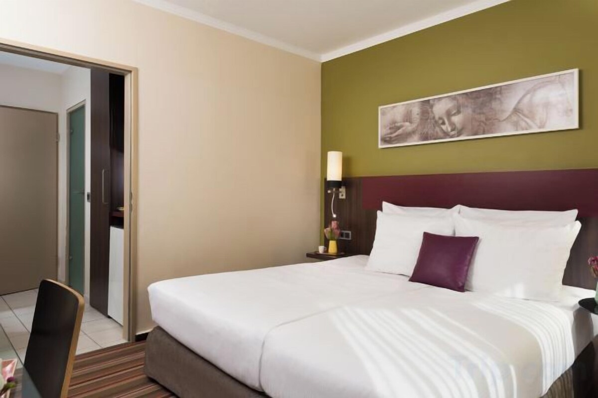 Habitació d'hotel amb un llit, una tauleta de nit, una làmpada i un quadre a la paret.