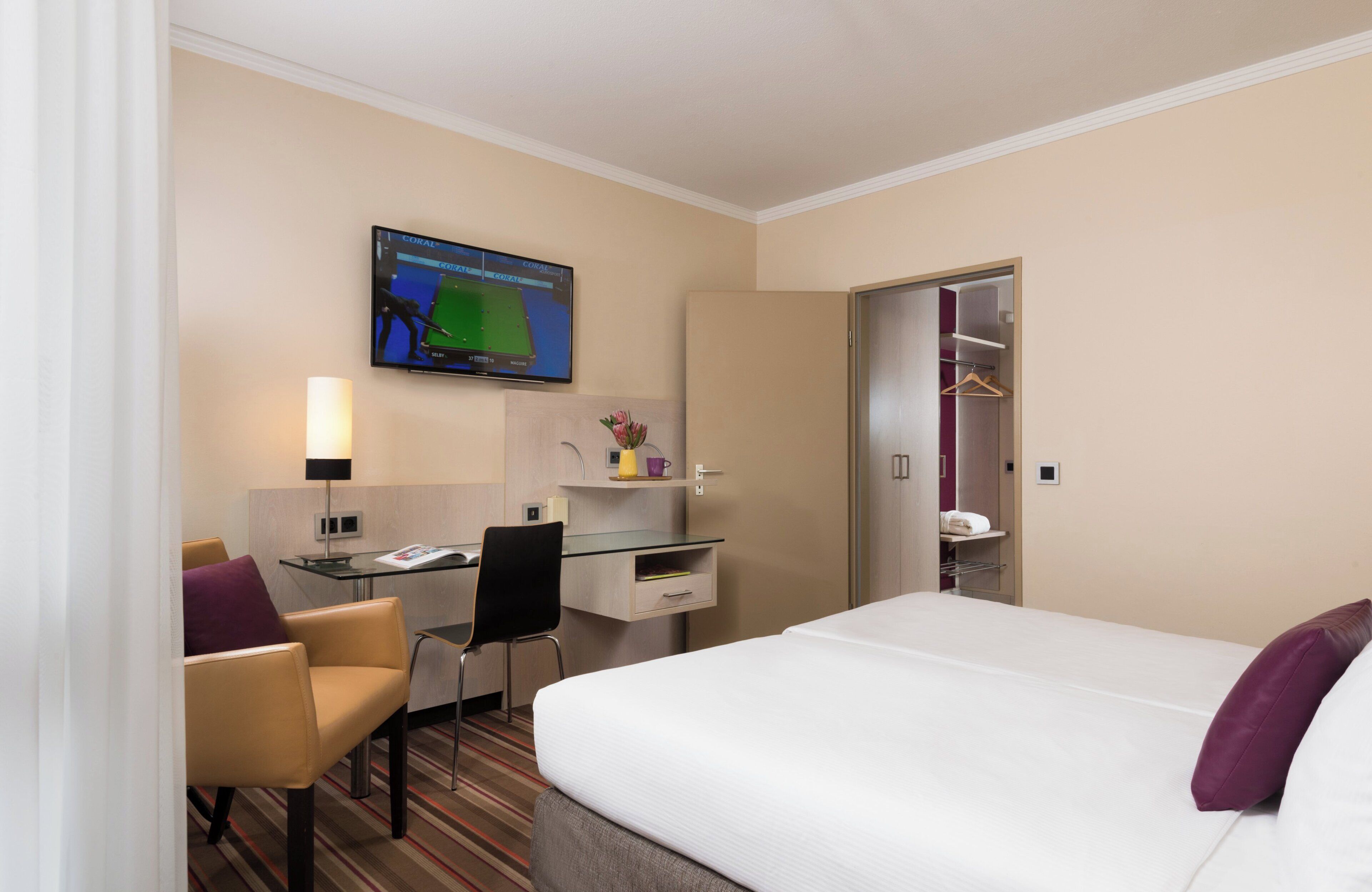 Una habitación de hotel con cama, escritorio con silla, televisión, armario y baño.