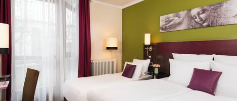 Habitación de hotel con dos camas, un escritorio, una silla, una lámpara y un cuadro en la pared.
