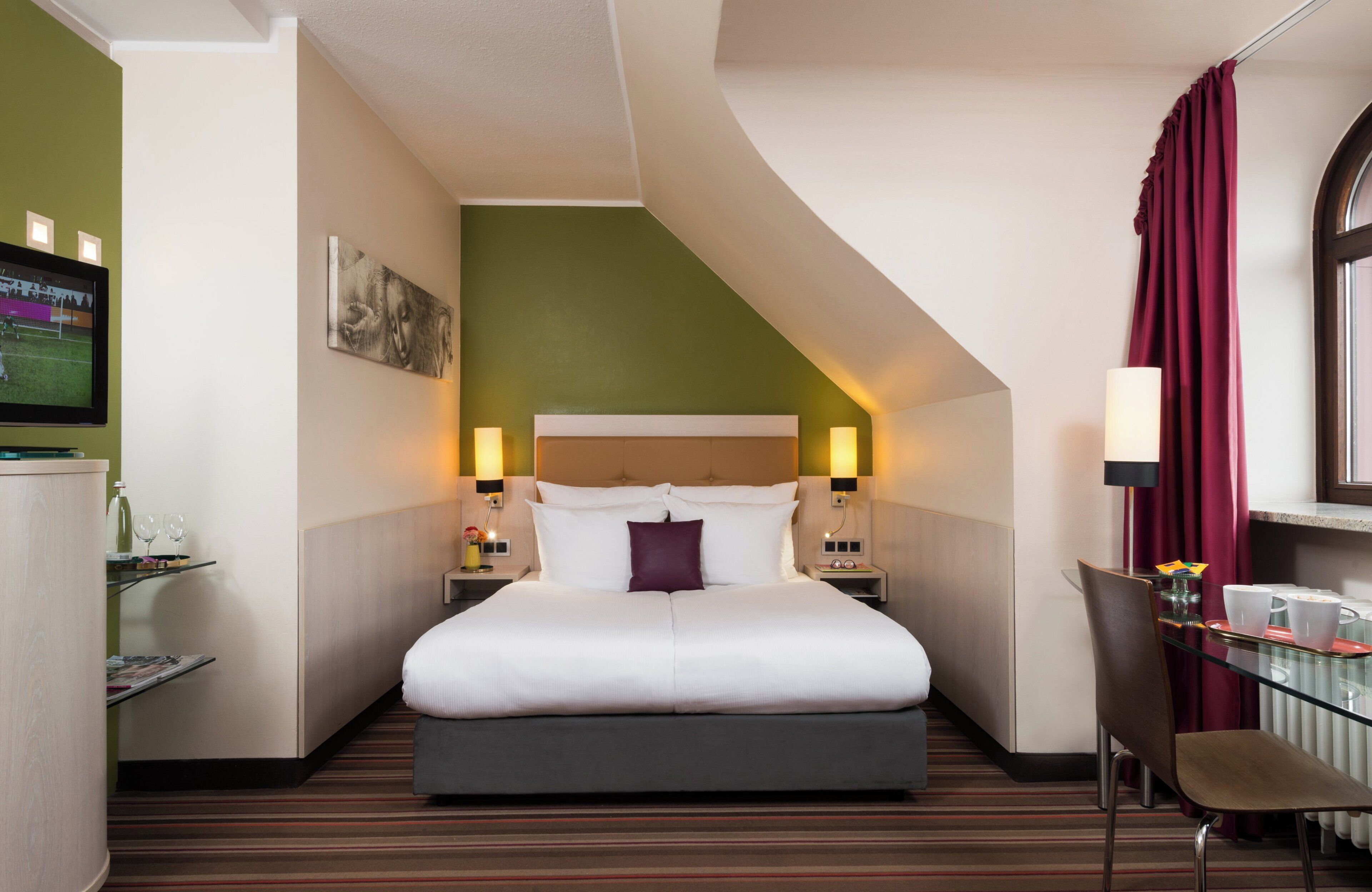 Una camera d'albergo con un letto grande, una scrivania con sedia, televisione e una finestra con tende.