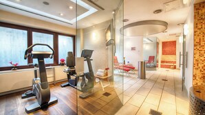 A modern hotel room with a large window, exercise equipment, a red chair, and a tiled bathroom. - Leonardo Hotel & Residenz München (Munich)