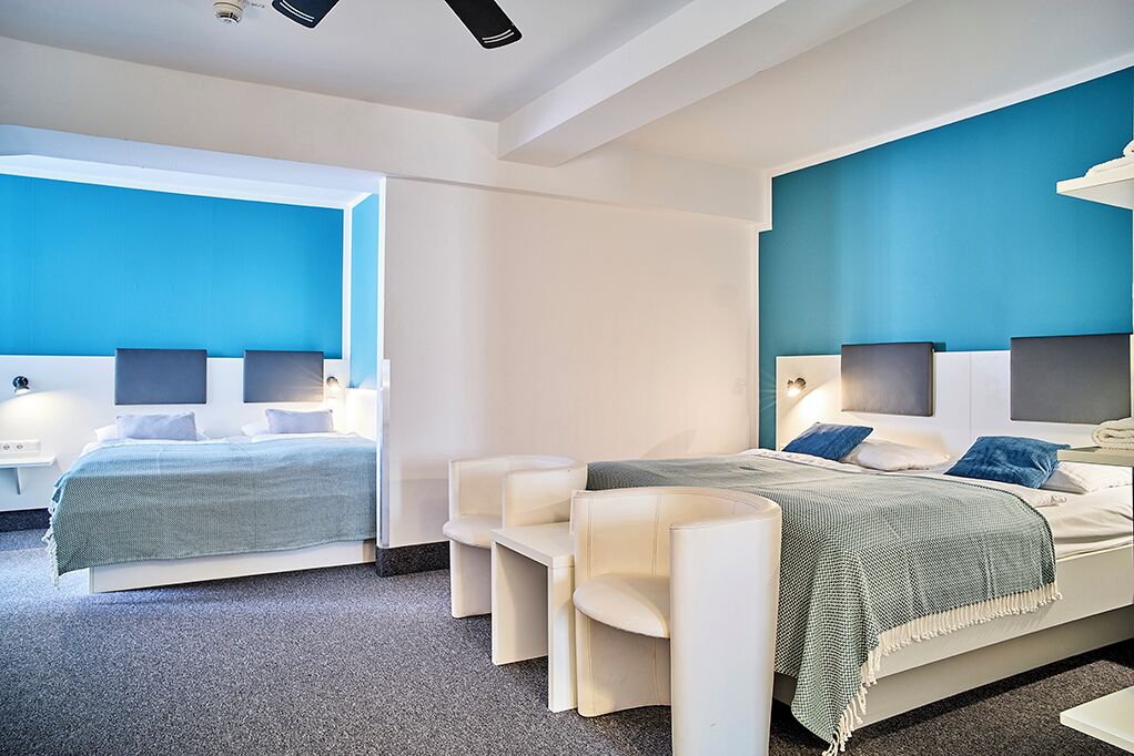 A modern hotel room with two beds, a seating area, and a large window.