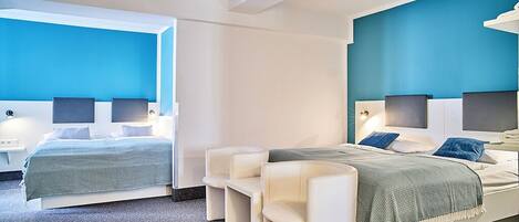 A modern hotel room with two beds, a seating area, and a large window.