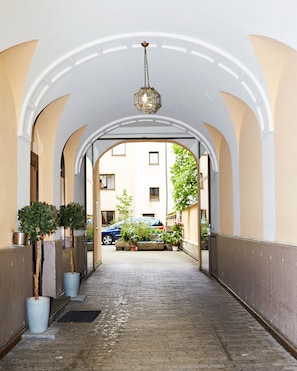 A corridor with arched ceilings, potted plants, and a car parked outside. - Brunnenhof City Center (Munich)
