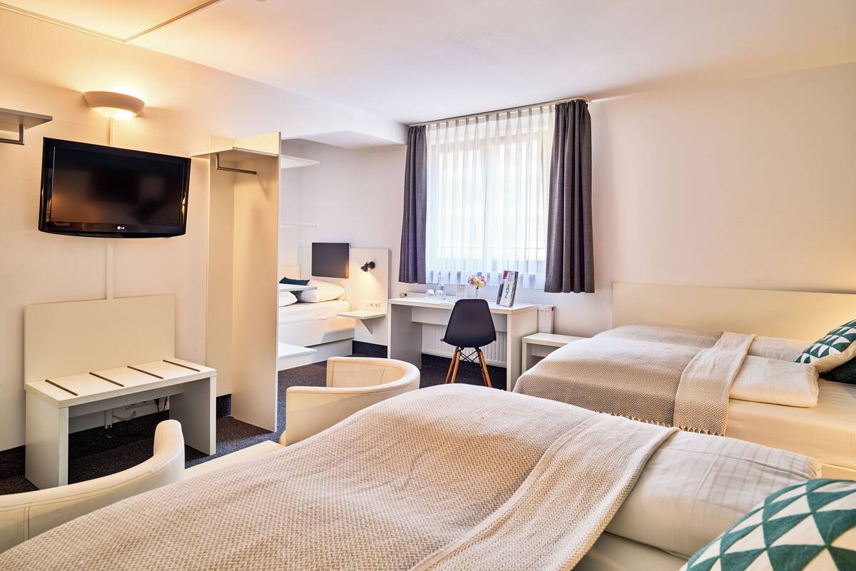 A hotel room with two beds, a desk, a chair, a TV, and a window with curtains.