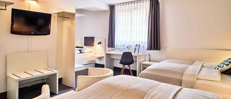 Habitación de hotel con dos camas, un escritorio, una silla, un televisor y una ventana con cortinas.