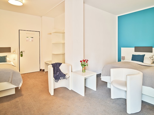 A modern hotel room with a bed, a chair, a small table with a vase of flowers, and a door with a lock. - Brunnenhof City Center (Munich)