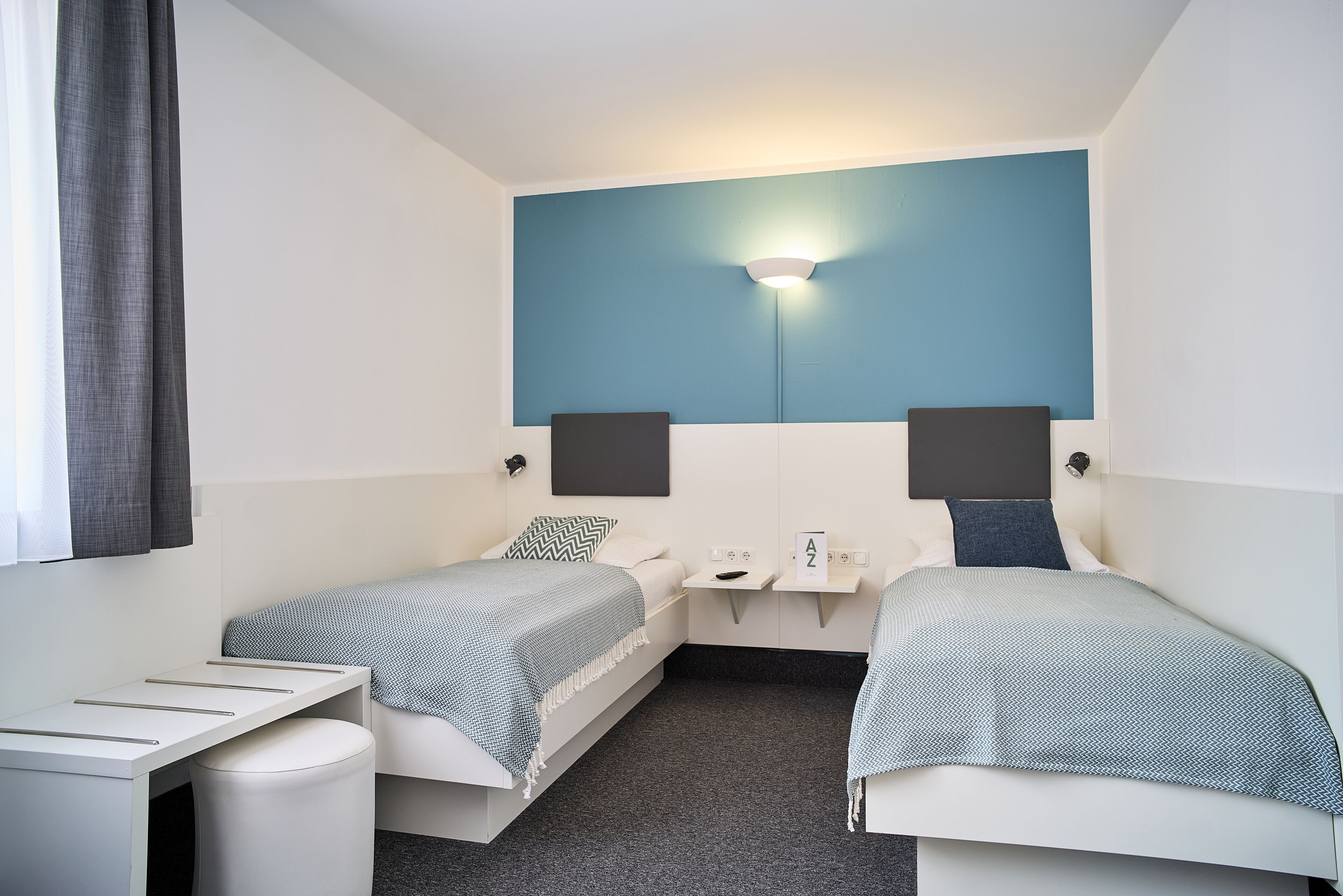 Ein kleines Hotelzimmer mit zwei Einzelbetten, einem Schreibtisch und einem kleinen Tisch.