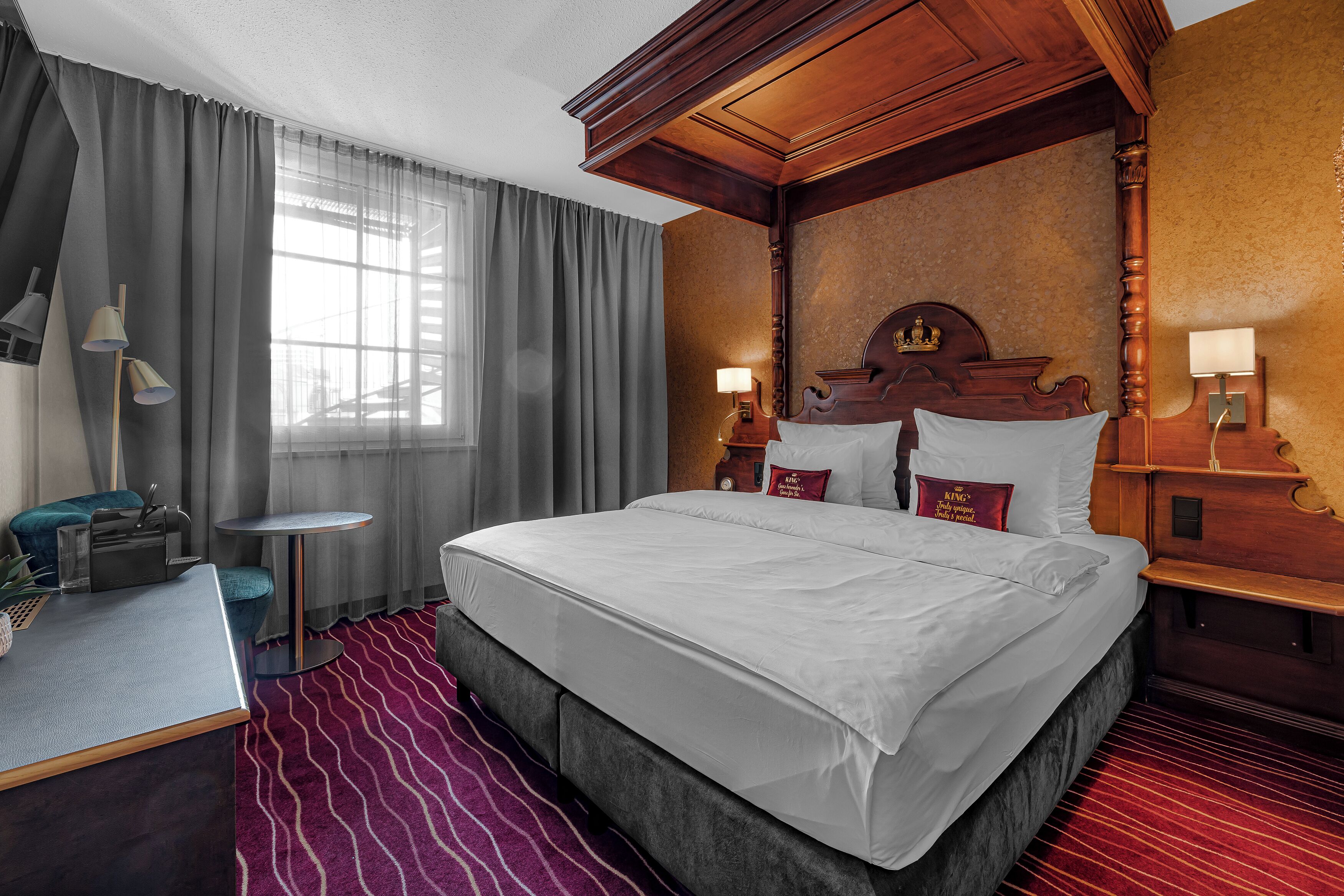 Ein Hotelzimmer mit einem großen Bett, einem Schreibtisch, einem Stuhl, einem kleinen Tisch und einem Fenster mit Vorhängen.