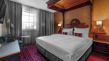 Ein Hotelzimmer mit einem großen Bett, einem Schreibtisch, einem Stuhl, einem kleinen Tisch und einem Fenster mit Vorhängen.