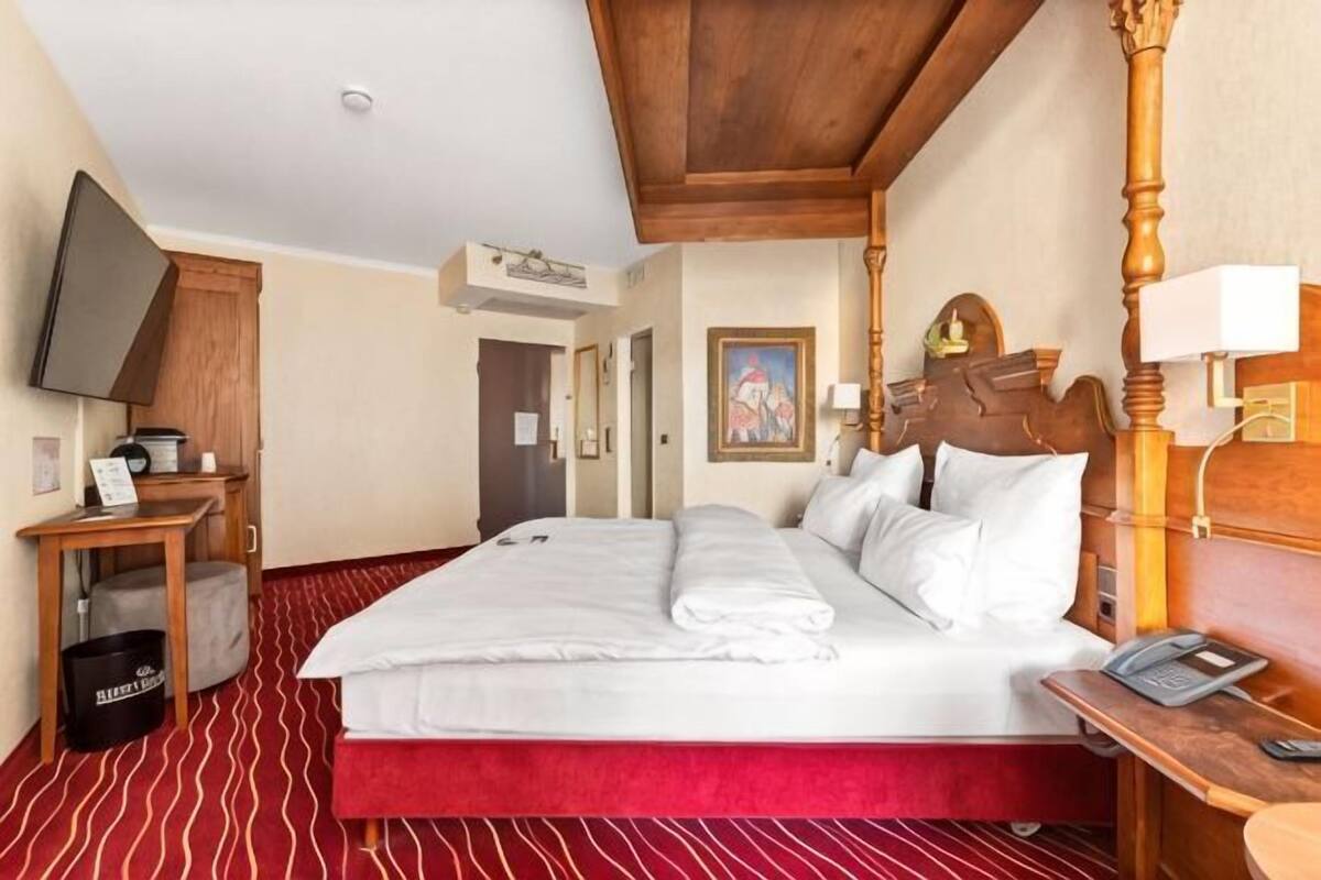 A hotel room with a large bed, a wooden headboard, a desk with a telephone, and a television on a stand.