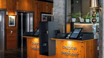 Tauleller de recepció amb indicació 'CHECK-IN + CHECK-OUT', un panell digital i una catifes amb el logotip 'KING'S HOTEL'.