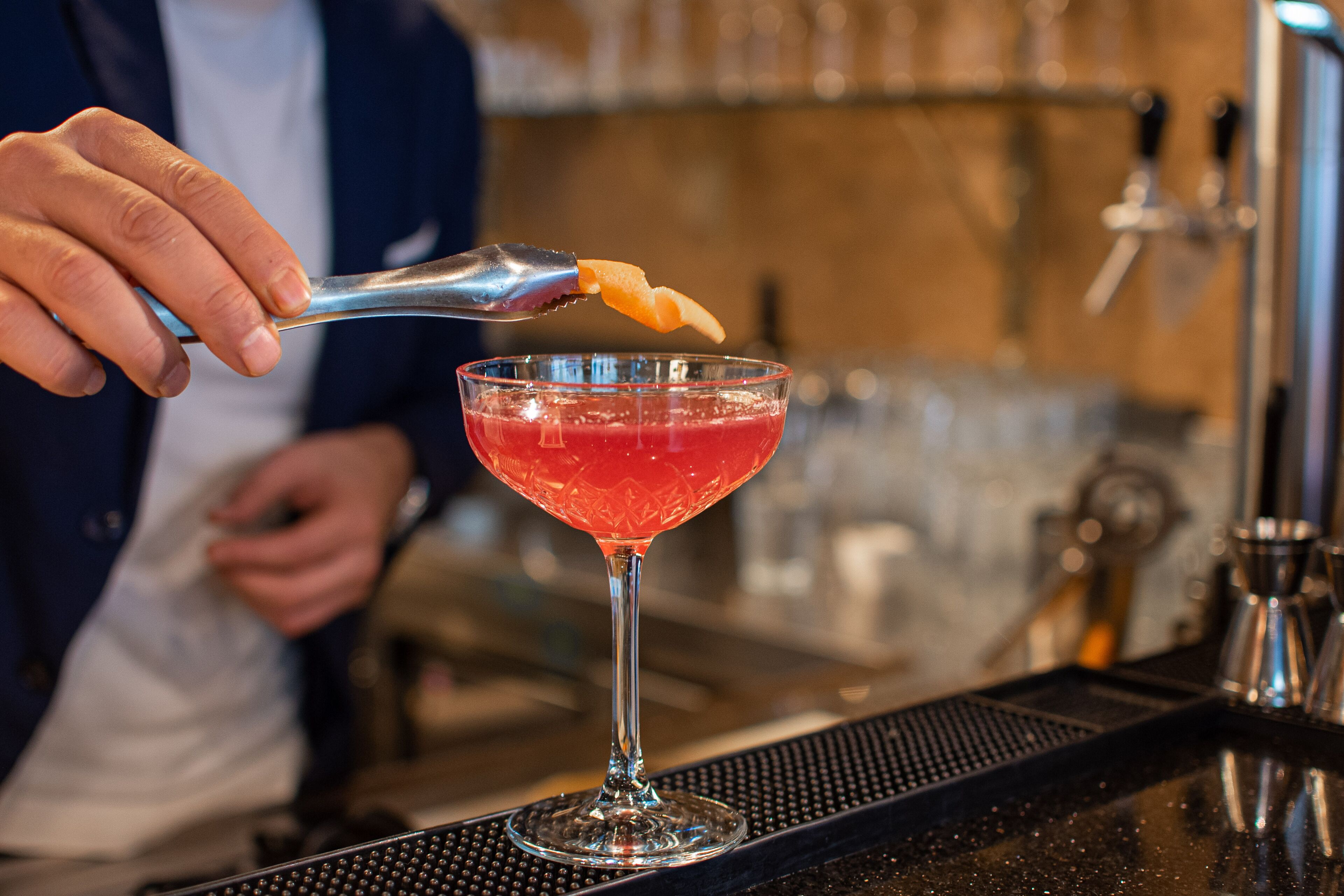 A bartender preparing a cocktail with a spoonful of a citrus garnish.