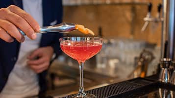A bartender preparing a cocktail with a spoonful of a citrus garnish.