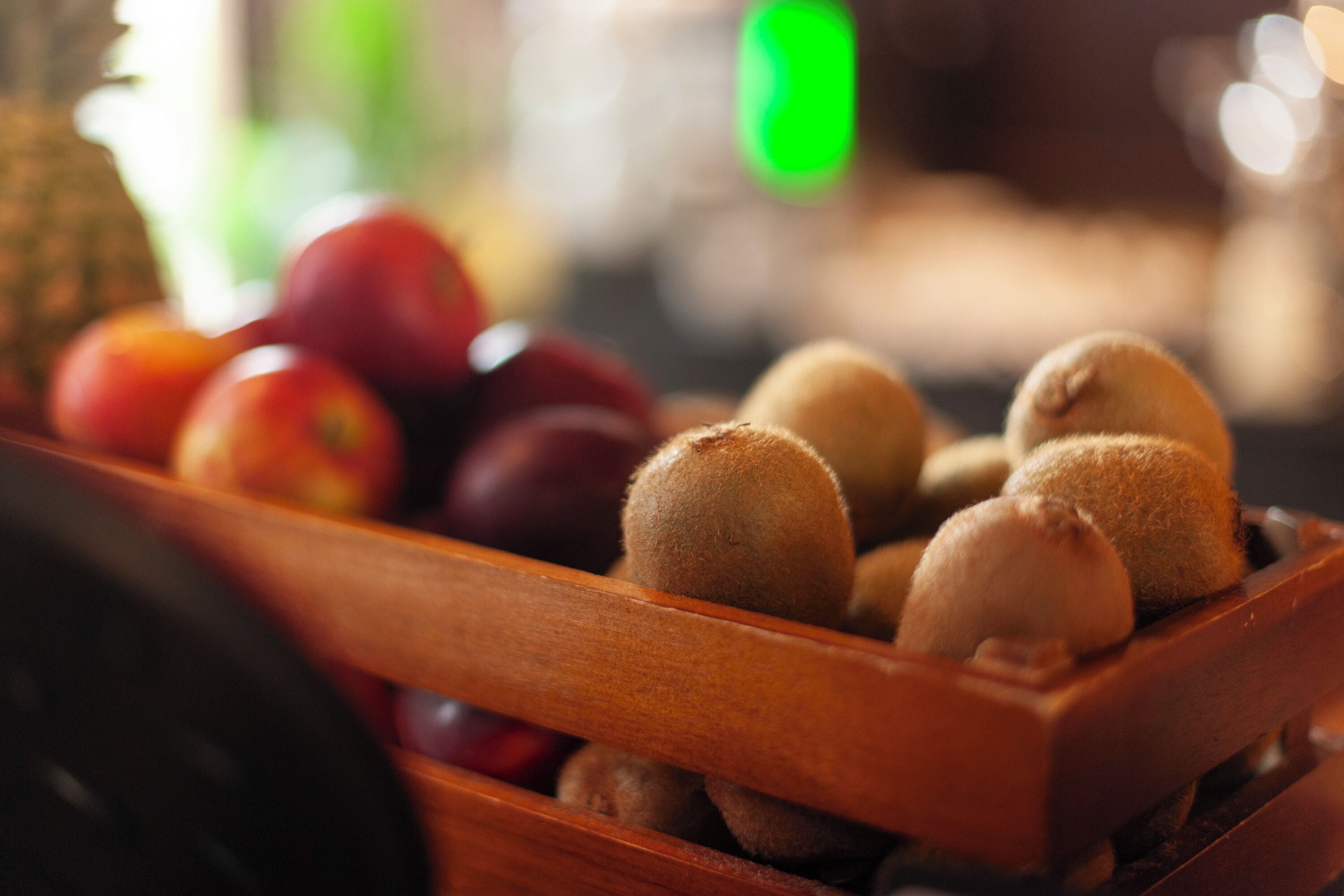 A wooden crate filled with kiwis and apples.