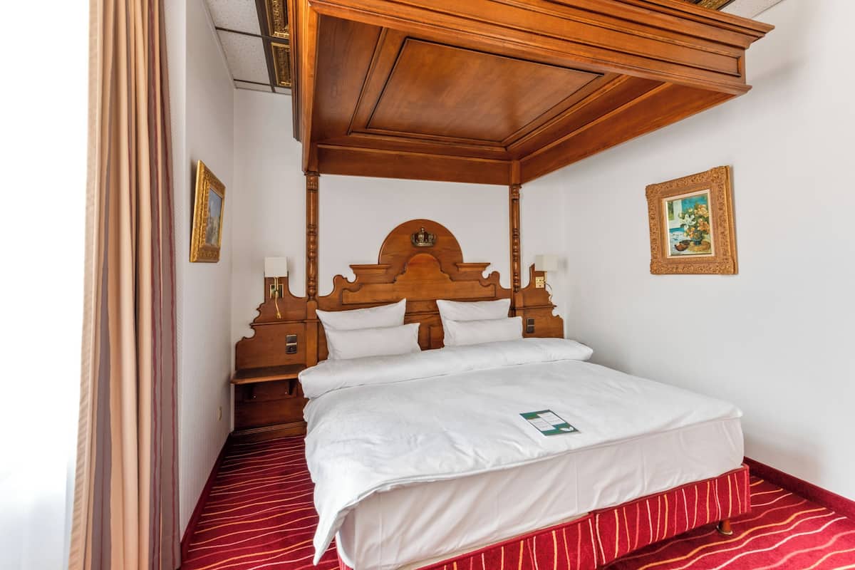 A neatly made bed with a wooden headboard, two bedside tables with lamps, and a red striped carpet.