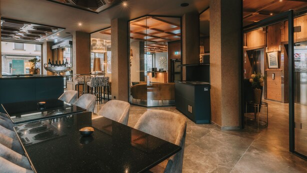 L’intérieur d’un restaurant moderne présente une table noire, des chaises rembourrées, un bar et une horloge bien visible.