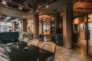 A modern restaurant interior with a black table, cushioned chairs, a bar area, and a visible clock. - KING's HOTEL First (Munich)
