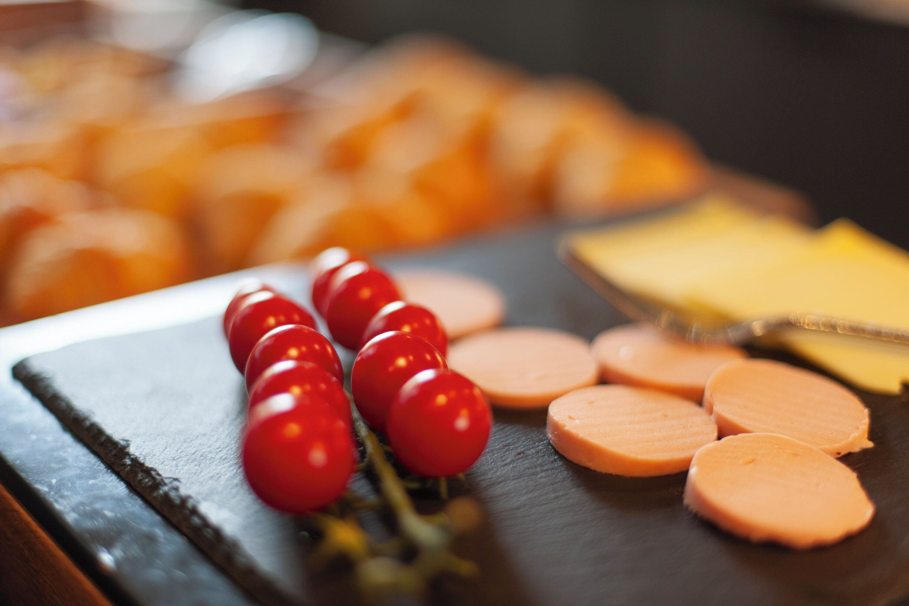 A charcuterie board with sliced meats, cheese, and cherry tomatoes.
