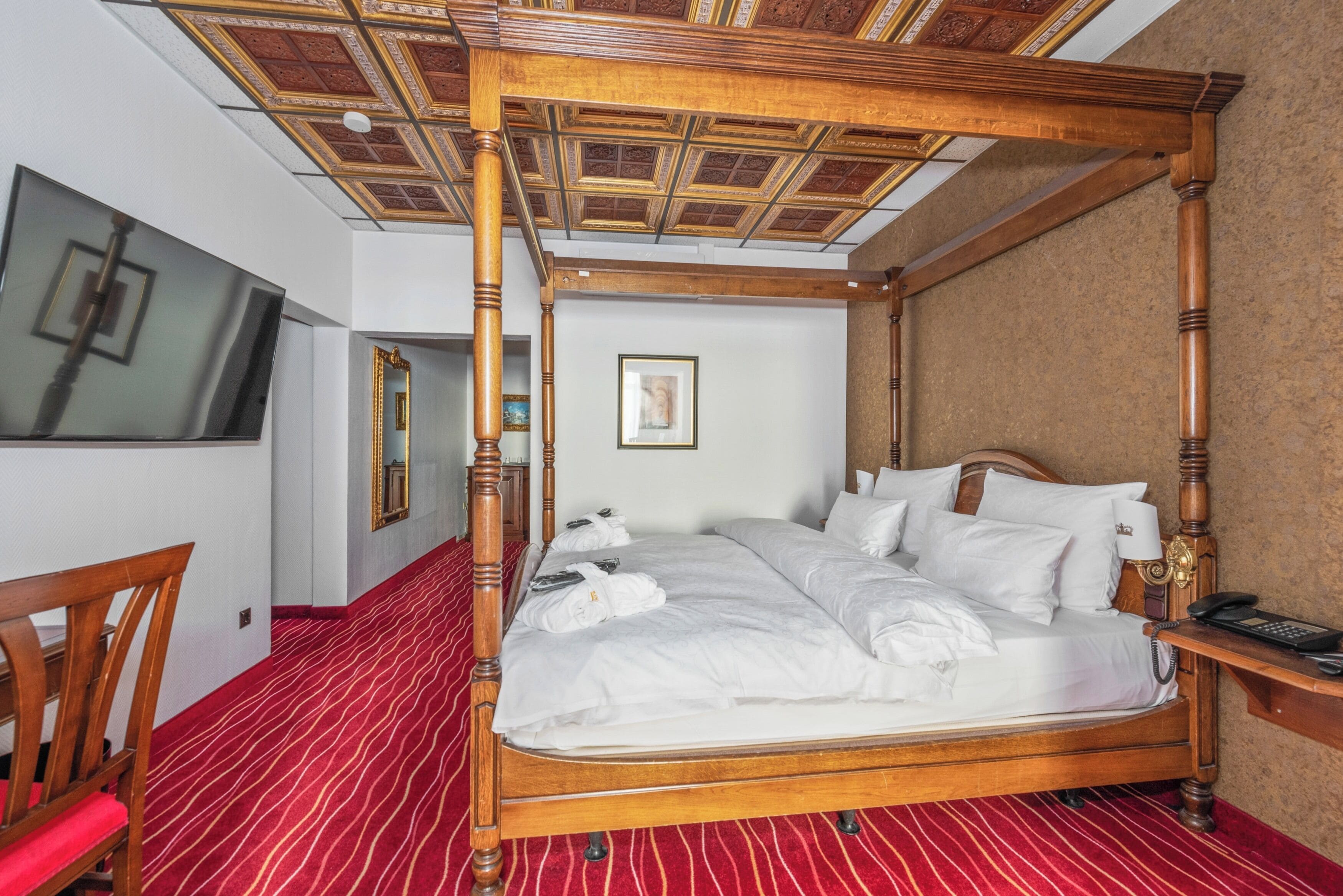 Una cama con dosel, ropa de cama blanca, cabecera de madera y suelo cubierto de alfombra roja.