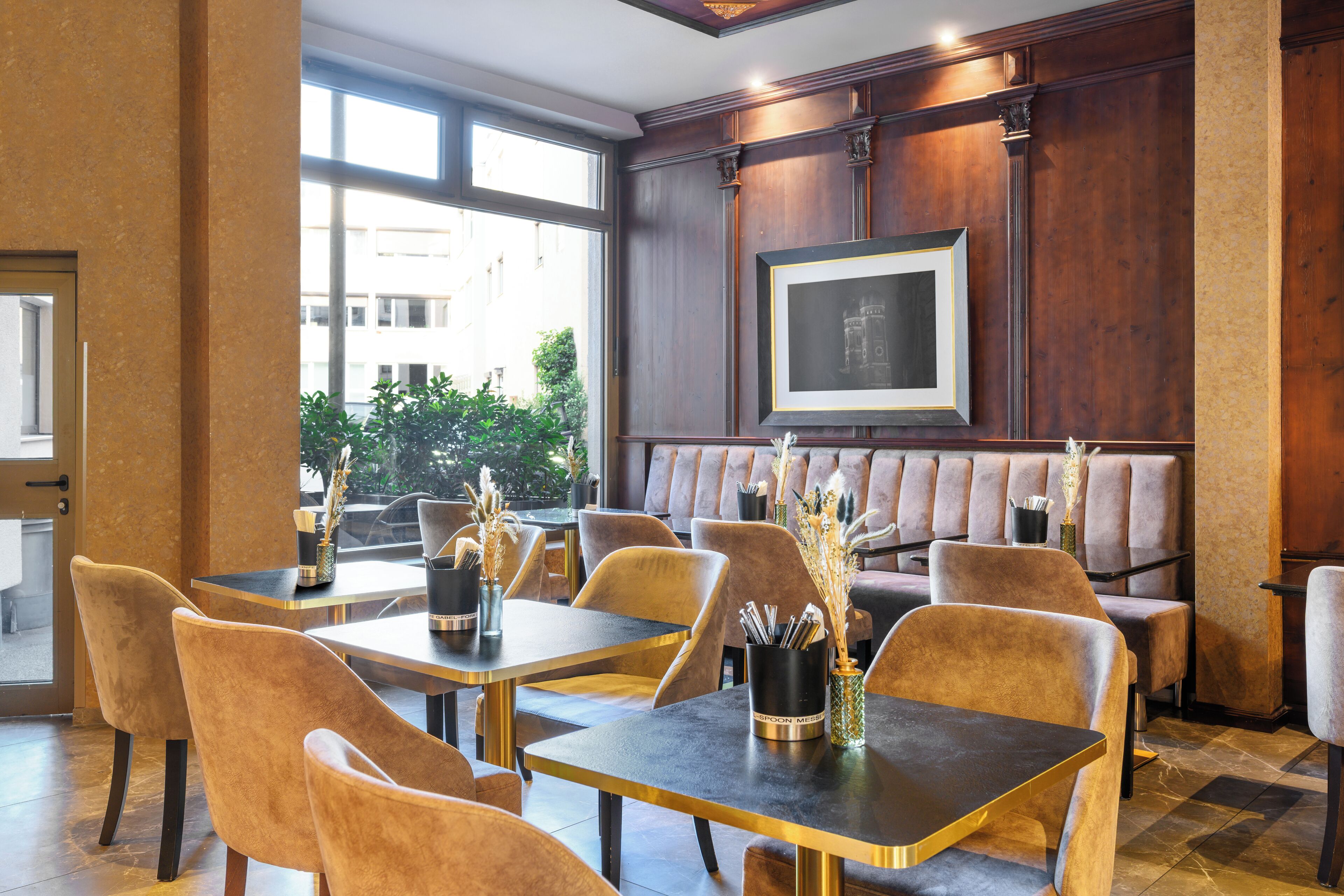 En restaurant med træpaneler, polstrede siddepladser og borde med sorte overflader og gyldne detaljer.
