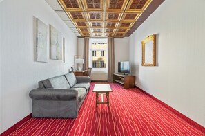 A hotel room with a grey sofa, a small white table, a TV, and a red striped carpet.