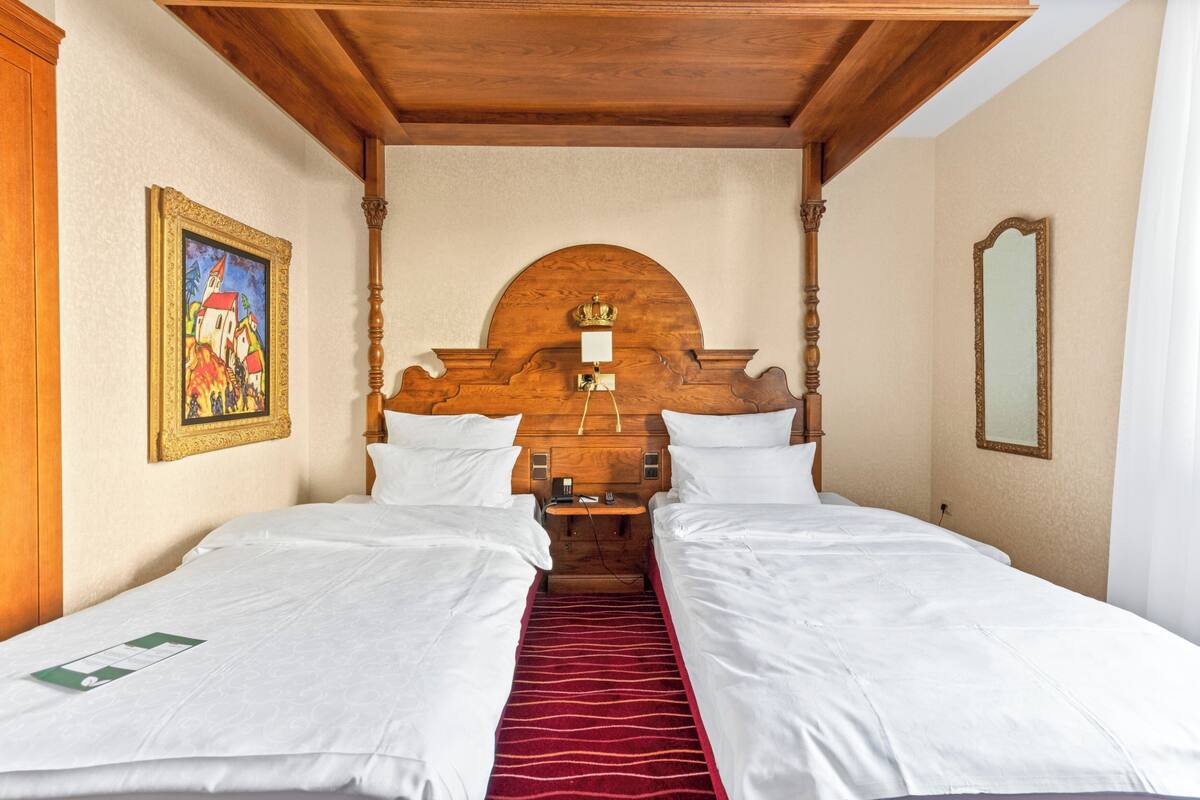 A hotel room with two single beds, wooden headboard, a red carpet, a painting on the wall, and a mirror.