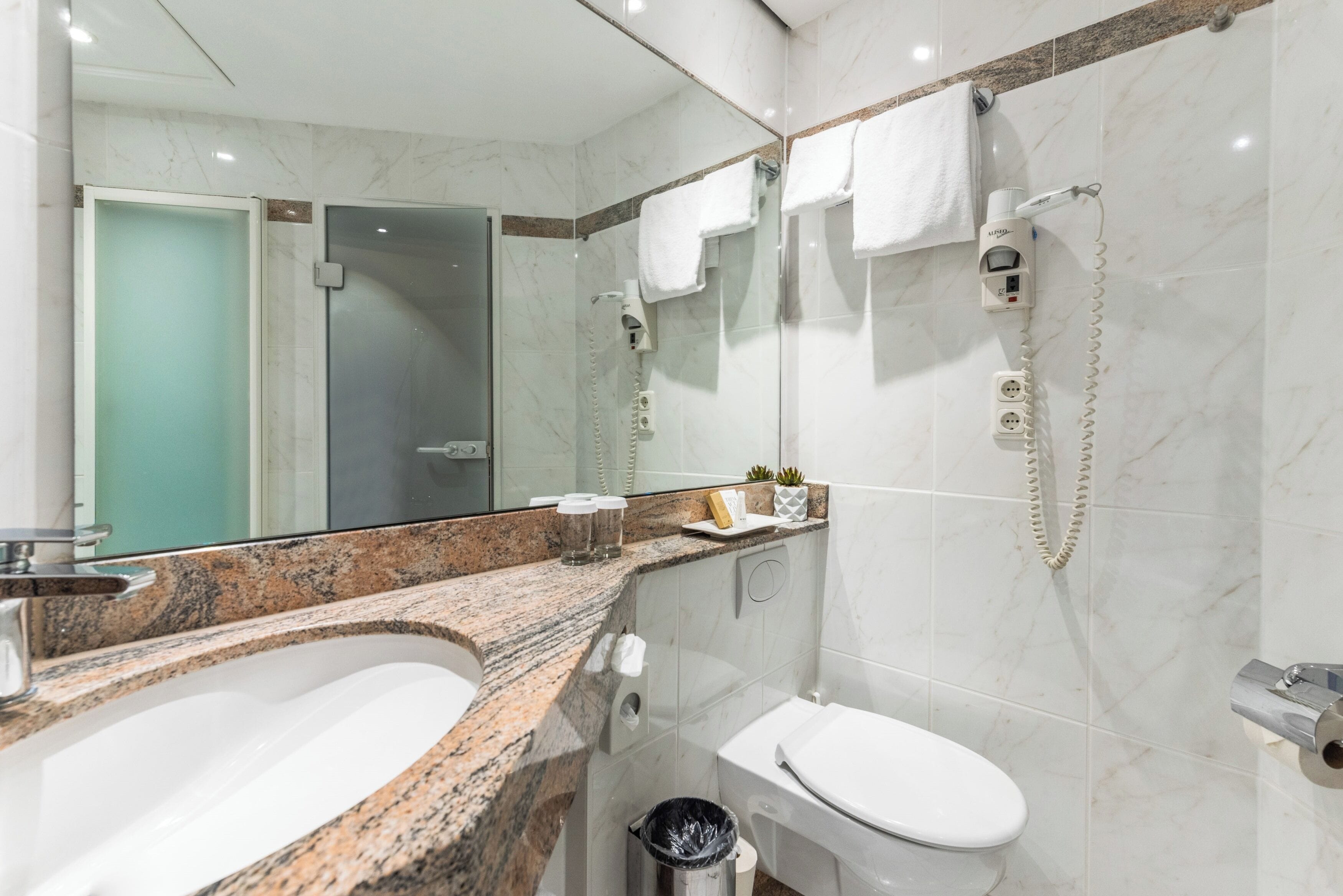 A modern bathroom with a granite countertop, a white sink, a toilet, and a glass-enclosed shower.