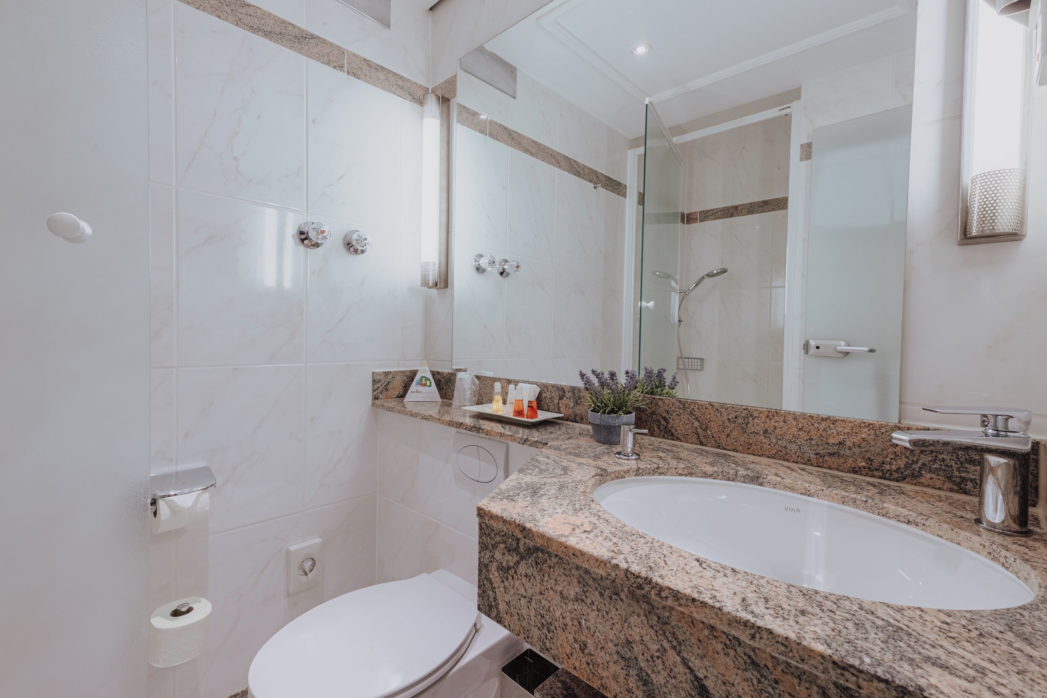 Un baño moderno con inodoro blanco, un lavabo grande y ducha con cerramiento de vidrio.