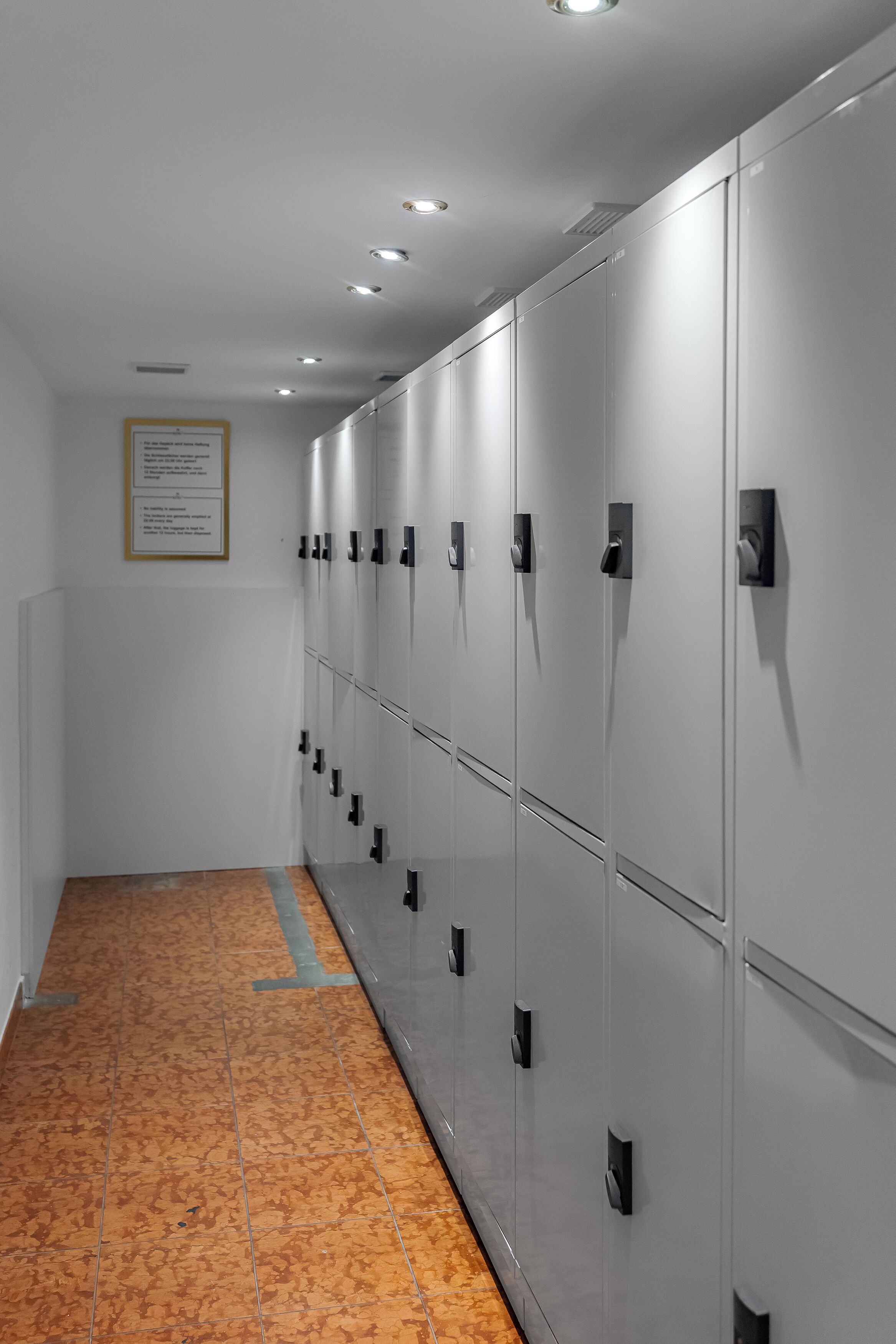 A row of lockers with a tiled floor and a framed notice on the wall.