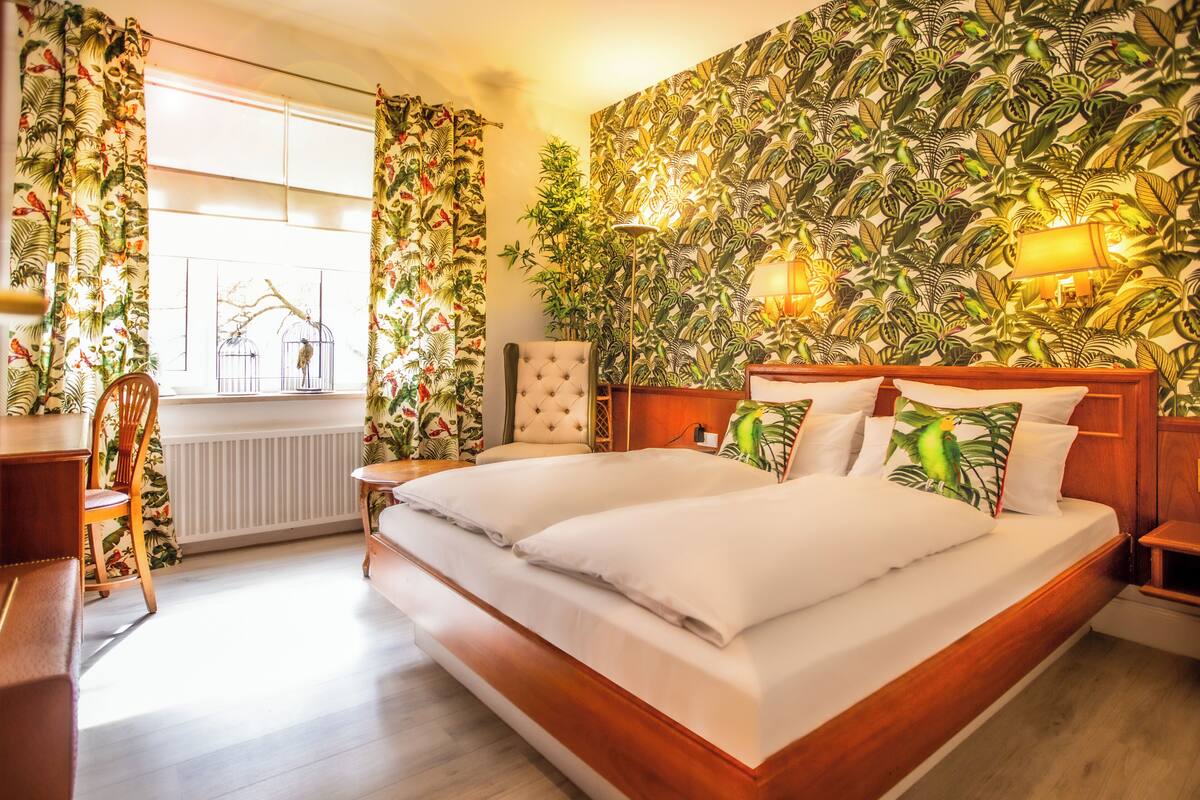 Un dormitorio con una cama grande, una silla, una mesa y una ventana con cortinas.