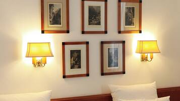 Habitación de hotel con dos camas, una mesita de noche, una lámpara y cuadros en la pared.