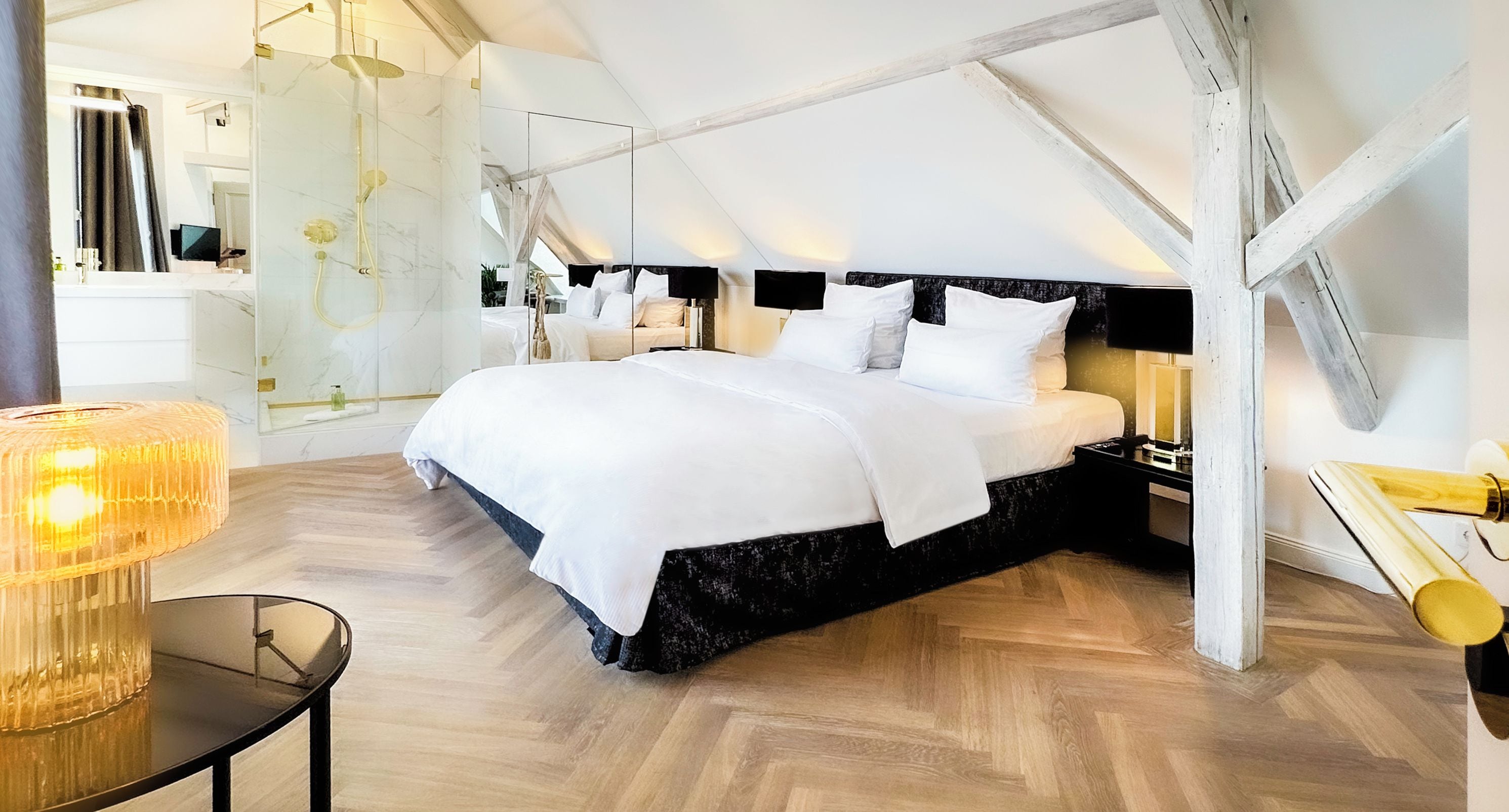 Un dormitorio moderno con una cama grande, cabina de ducha de vidrio y suelo de madera con diseño de espiga.