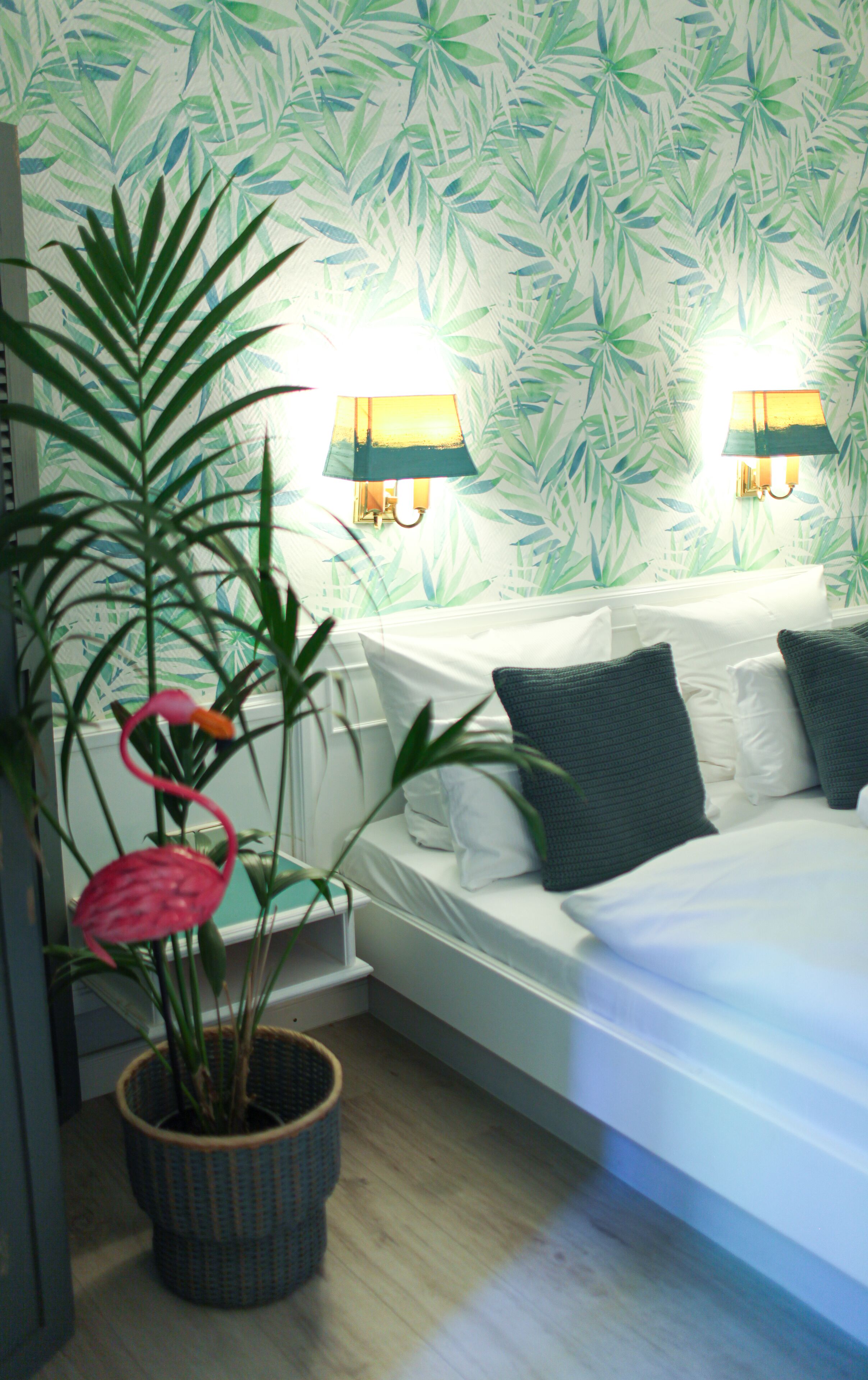 Un dormitorio con una cama, dos lámparas de pared y una planta en maceta con una flor rosa.