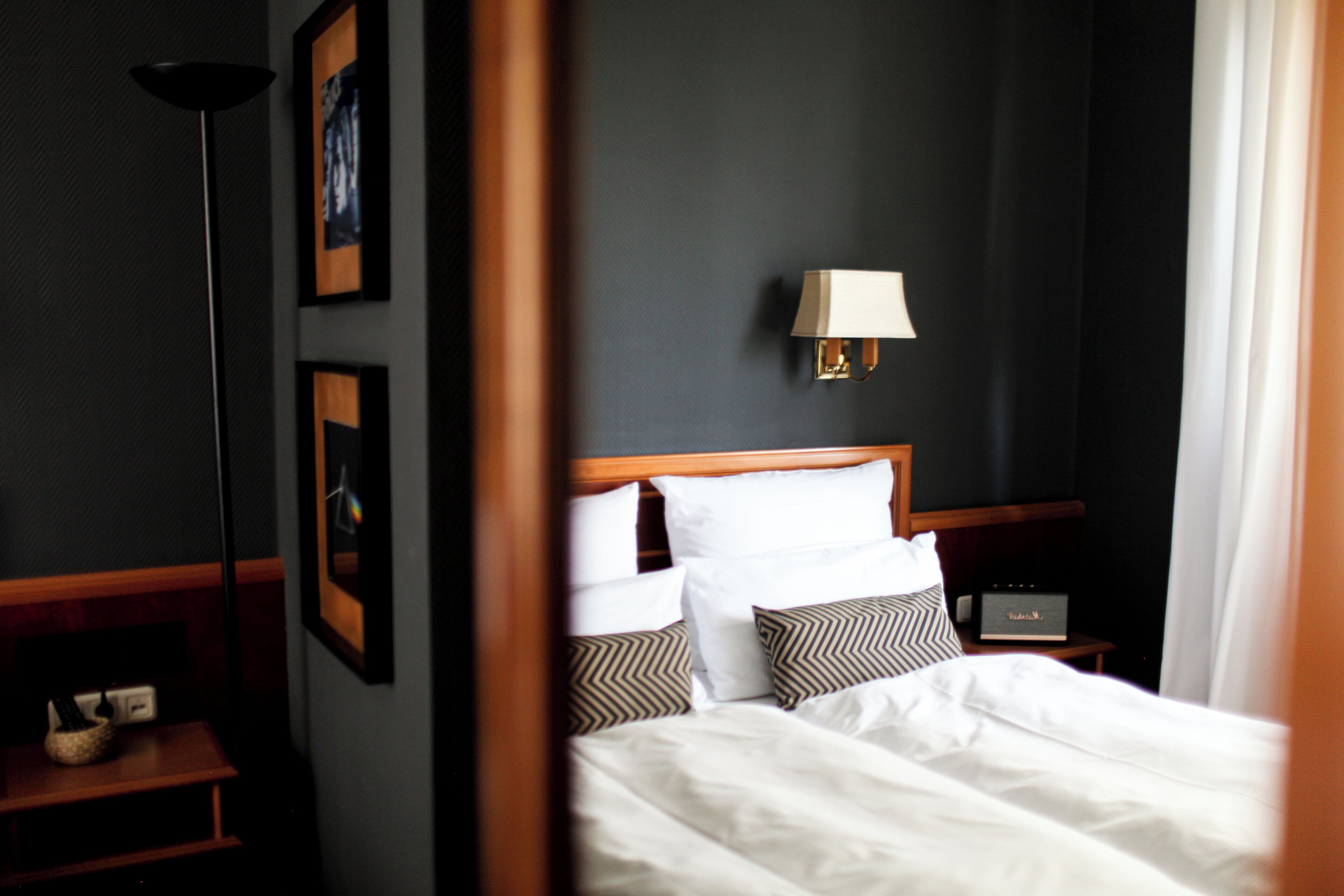 A hotel room with a neatly made bed, a bedside table with a lamp, and framed pictures on the wall.