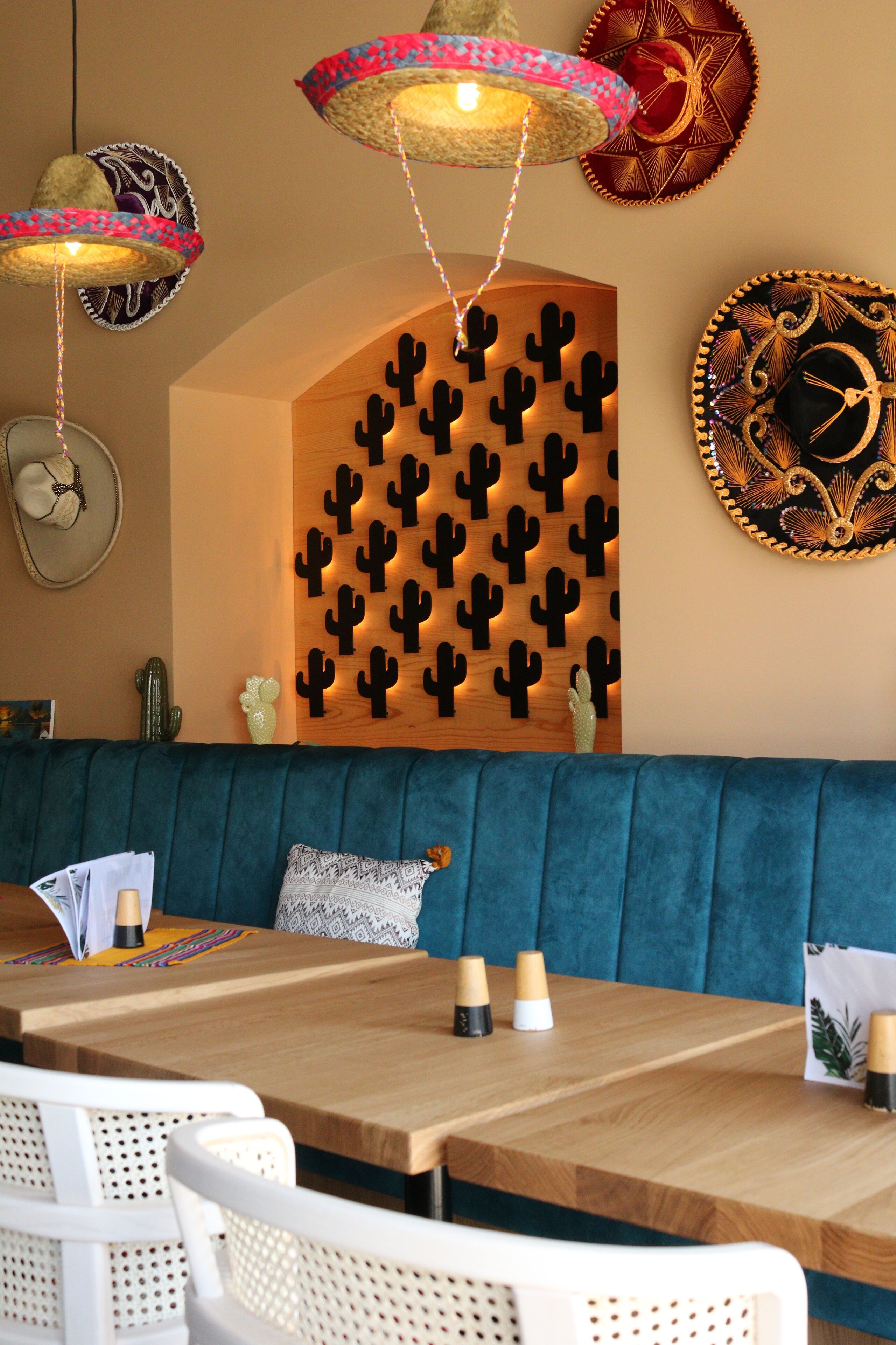 Ein Essbereich mit Holztisch, blau gepolstertem Bänkchen und einer Wand mit dekorativen Kakteen.