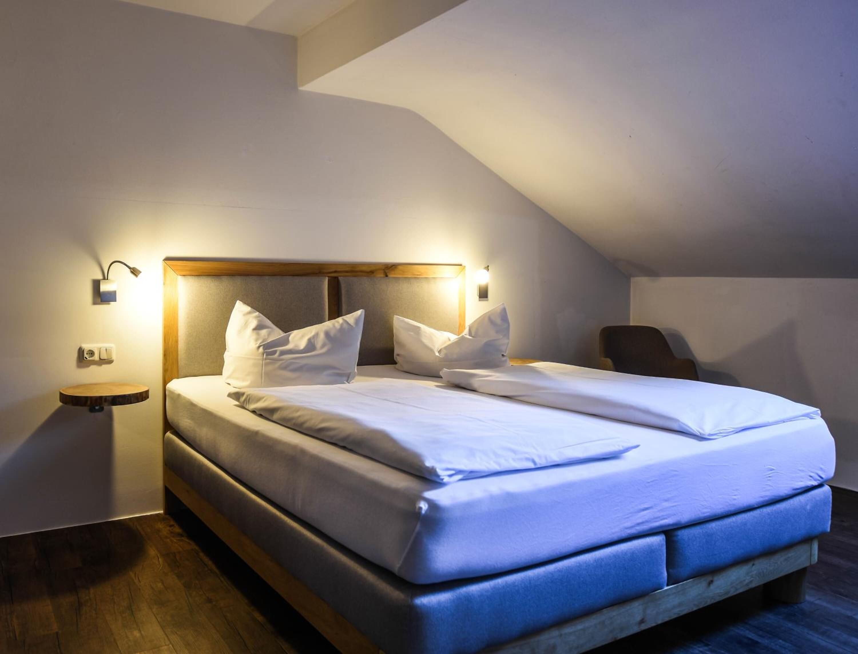 A neatly made bed with white linens, a wooden headboard, and two bedside lamps.