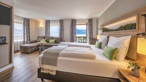 A modern hotel room with a large bed, a sofa, and a balcony with a view of the mountains. - Seehotel zur Post (Tegernsee)