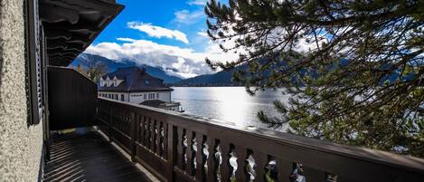 Ein Holzbalkon mit Geländer, der auf einen See und Berge blickt.