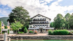 A two-story building with a balcony, located beside a body of water. - Seehotel zur Post (Tegernsee)