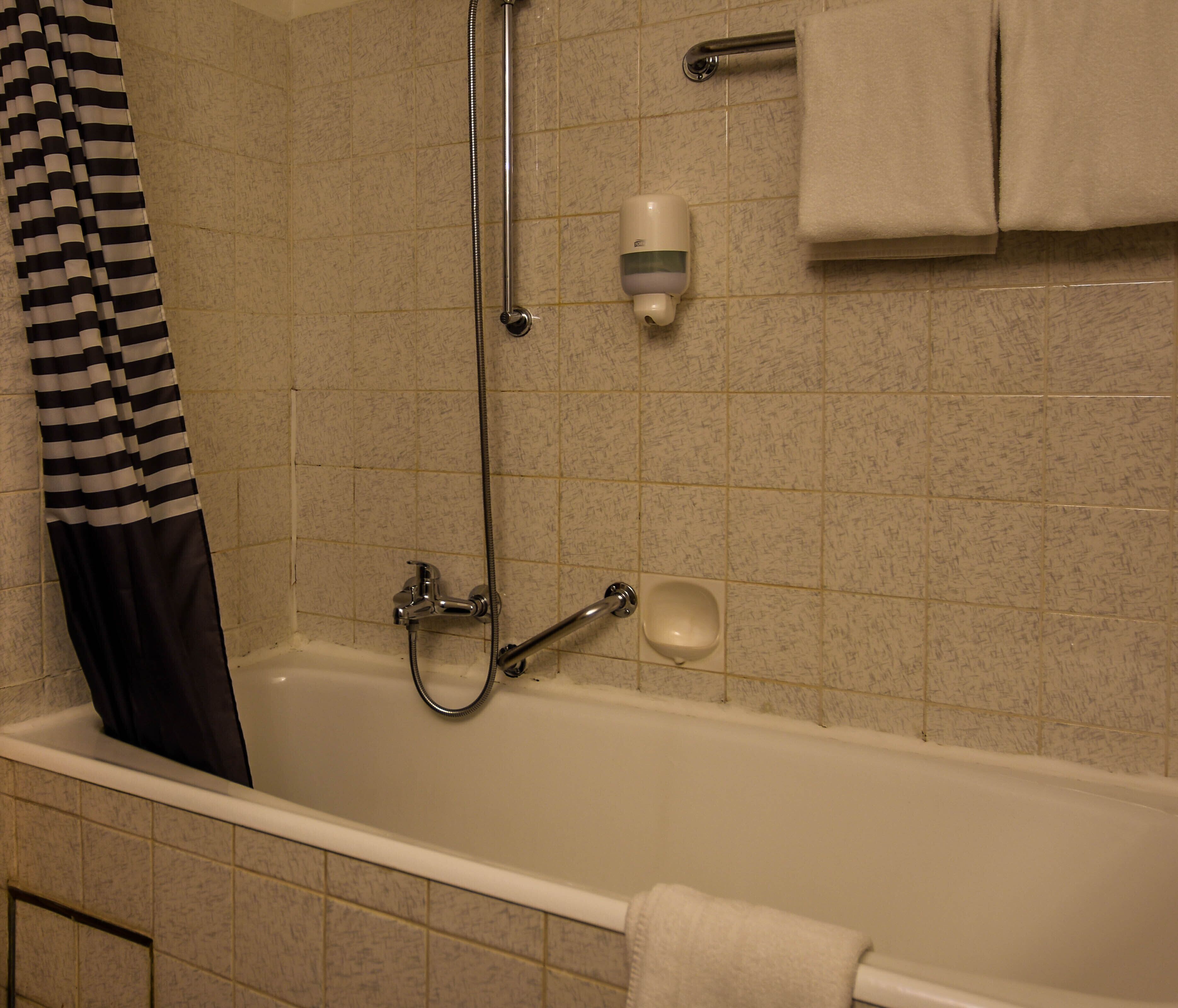 Una bañera con ducha, un cabezal de ducha y un dispensador de jabón.