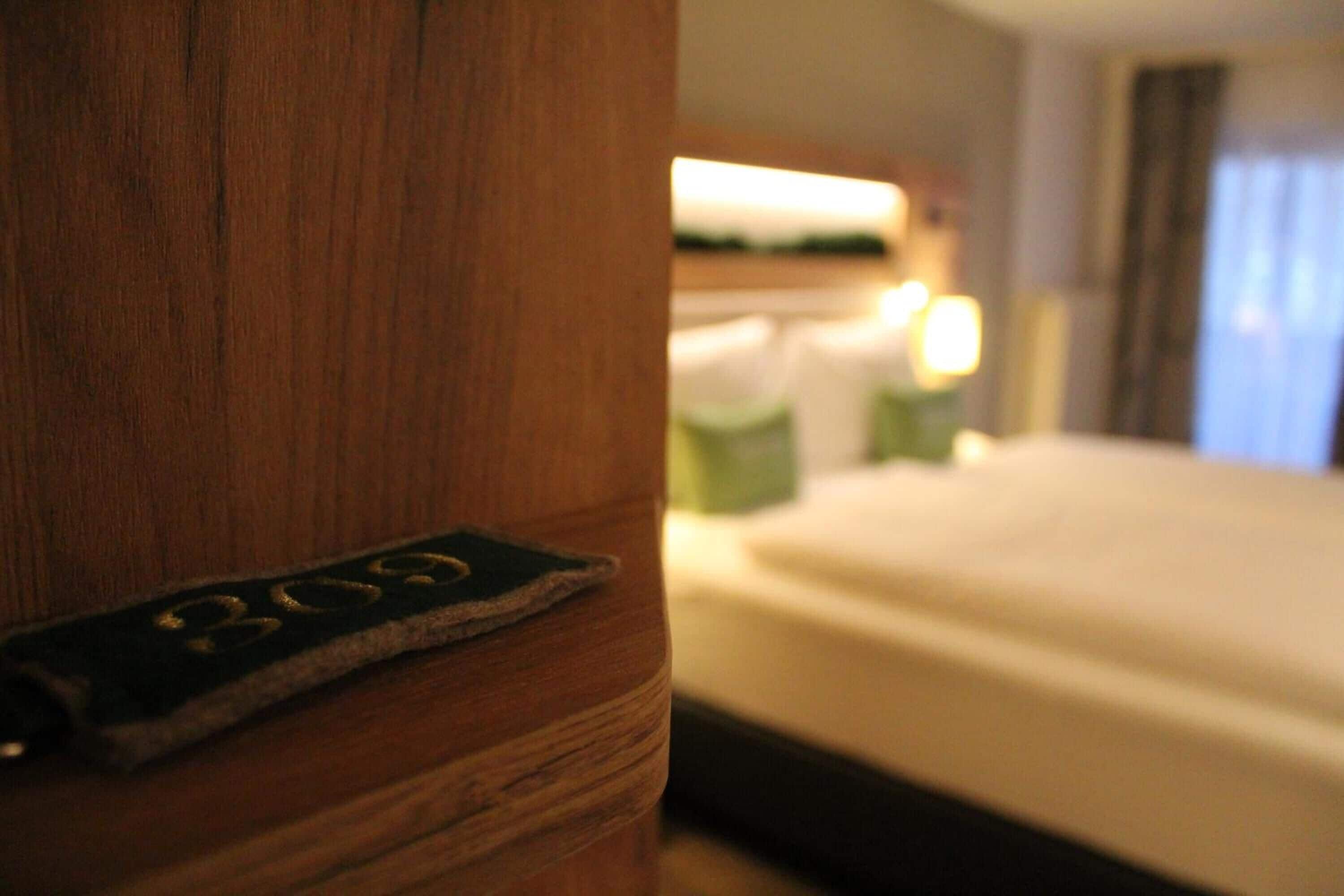 Una habitación de hotel con cabecera de madera, cama con ropa de cama blanca y mesita de noche con lámpara.