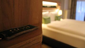 Una habitación de hotel con cabecera de madera, cama con ropa de cama blanca y mesita de noche con lámpara.