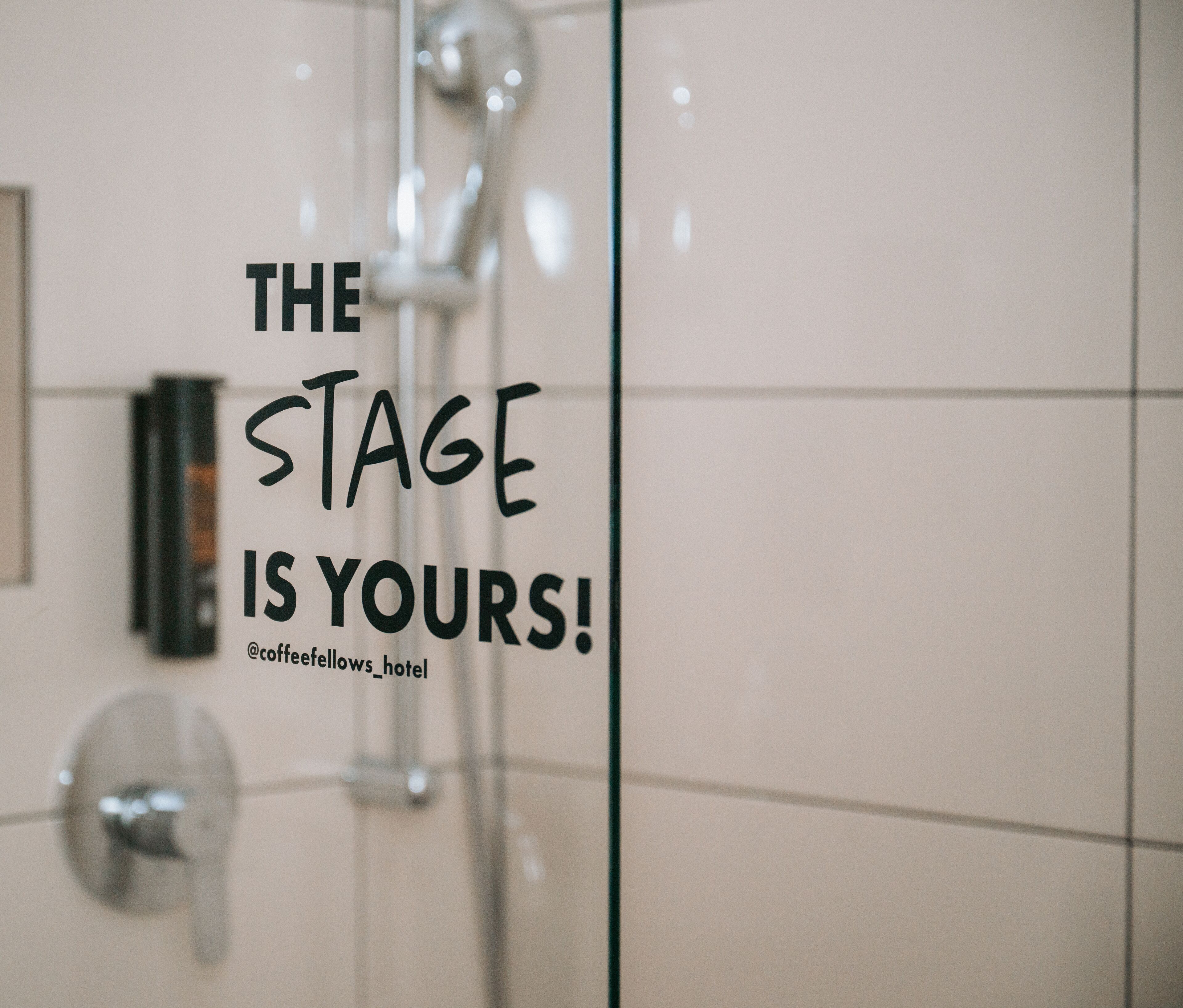 A bathroom with a glass shower enclosure and a motivational quote on the wall.