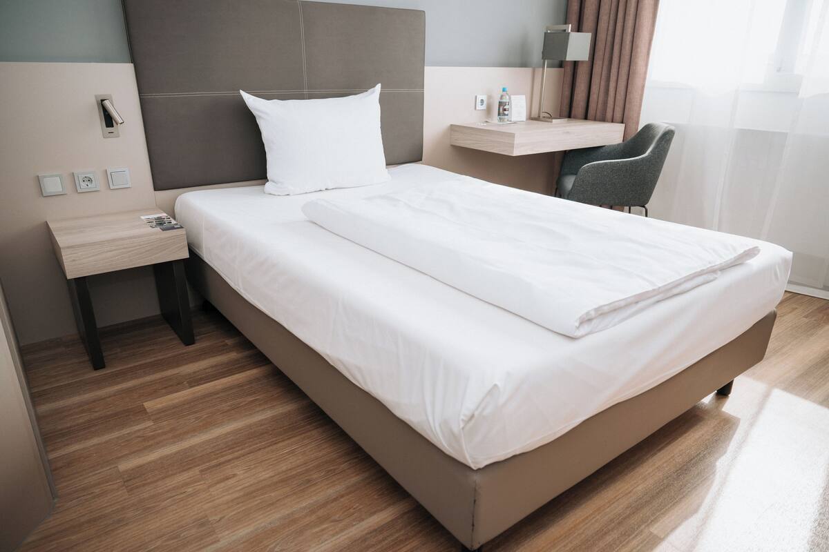 A modern hotel room with a large bed, a bedside table, a chair, and a small desk.