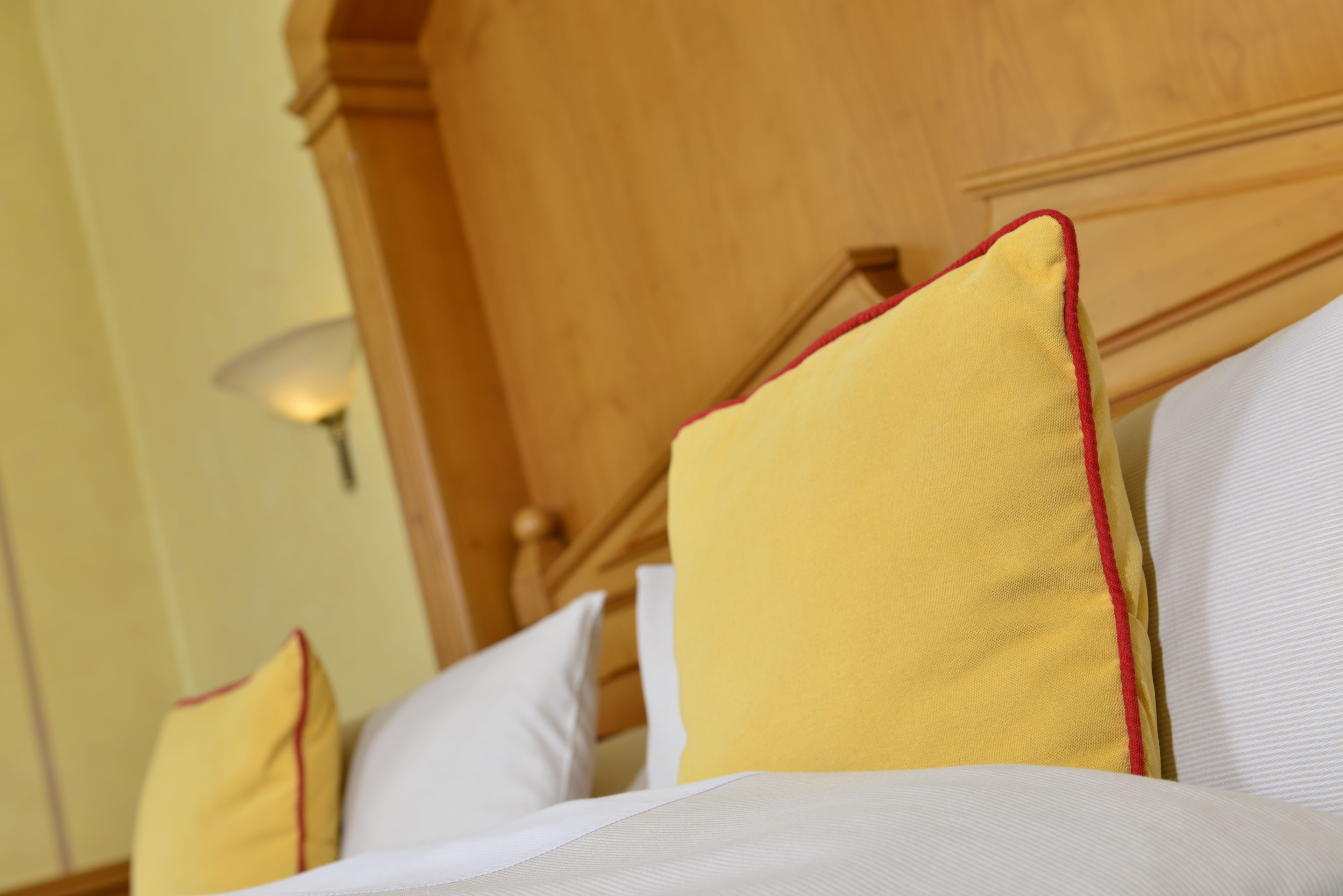 A bed with white and yellow pillows, a wooden headboard, and a wall-mounted lamp.
