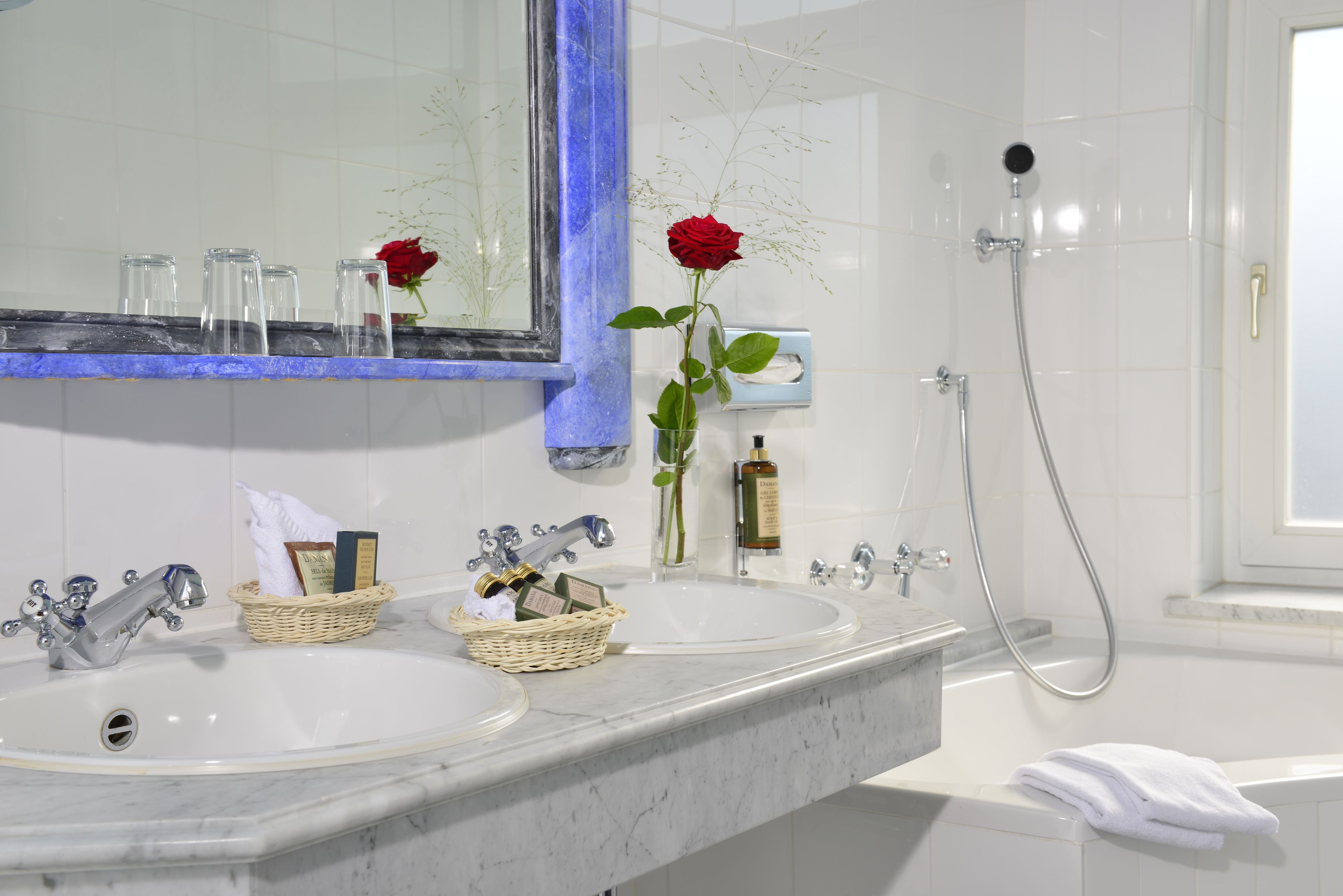 A bathroom with two sinks, a mirror, a shower, and a vase with a rose.